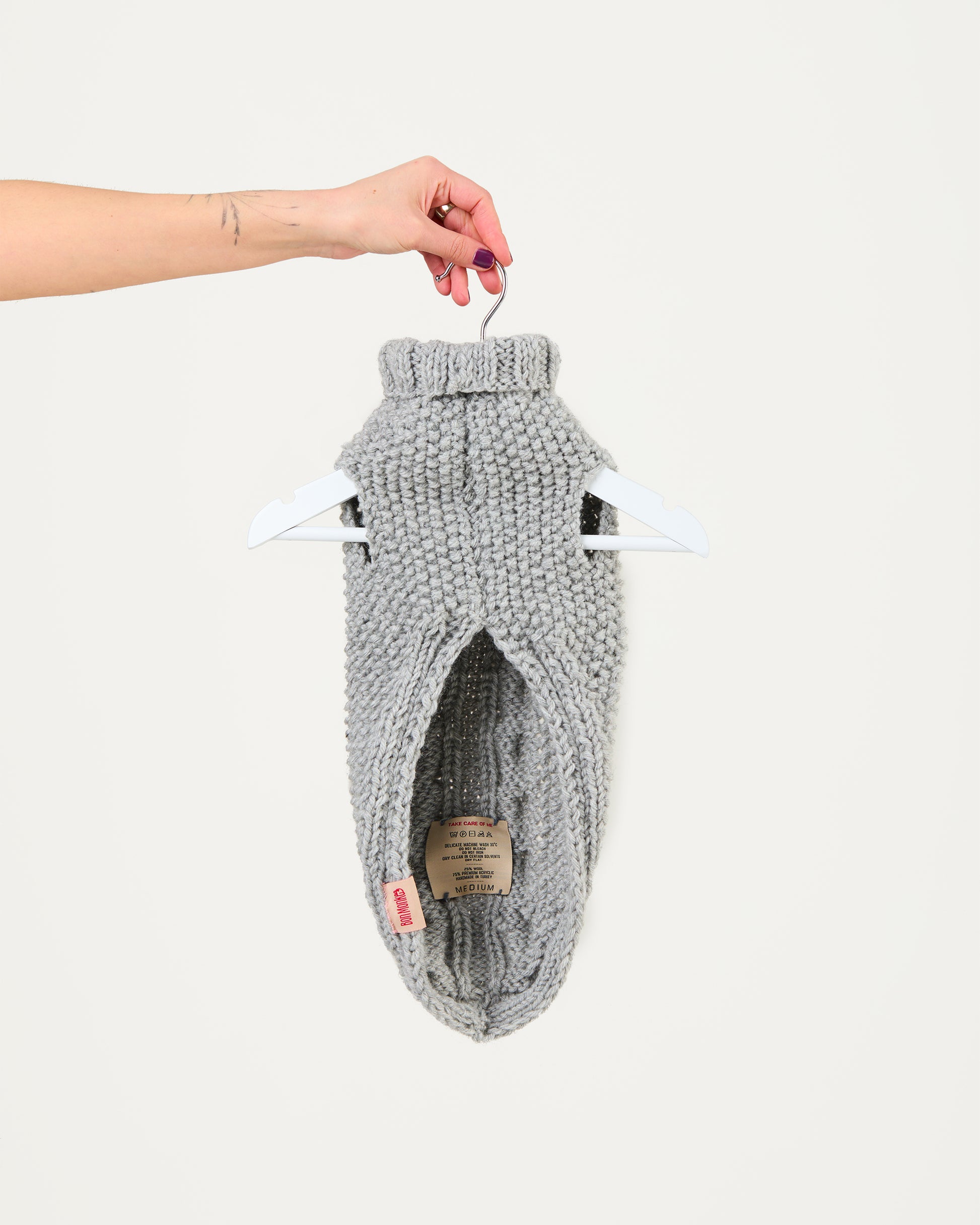 Gray knitted dog sweater on a hanger against a white background