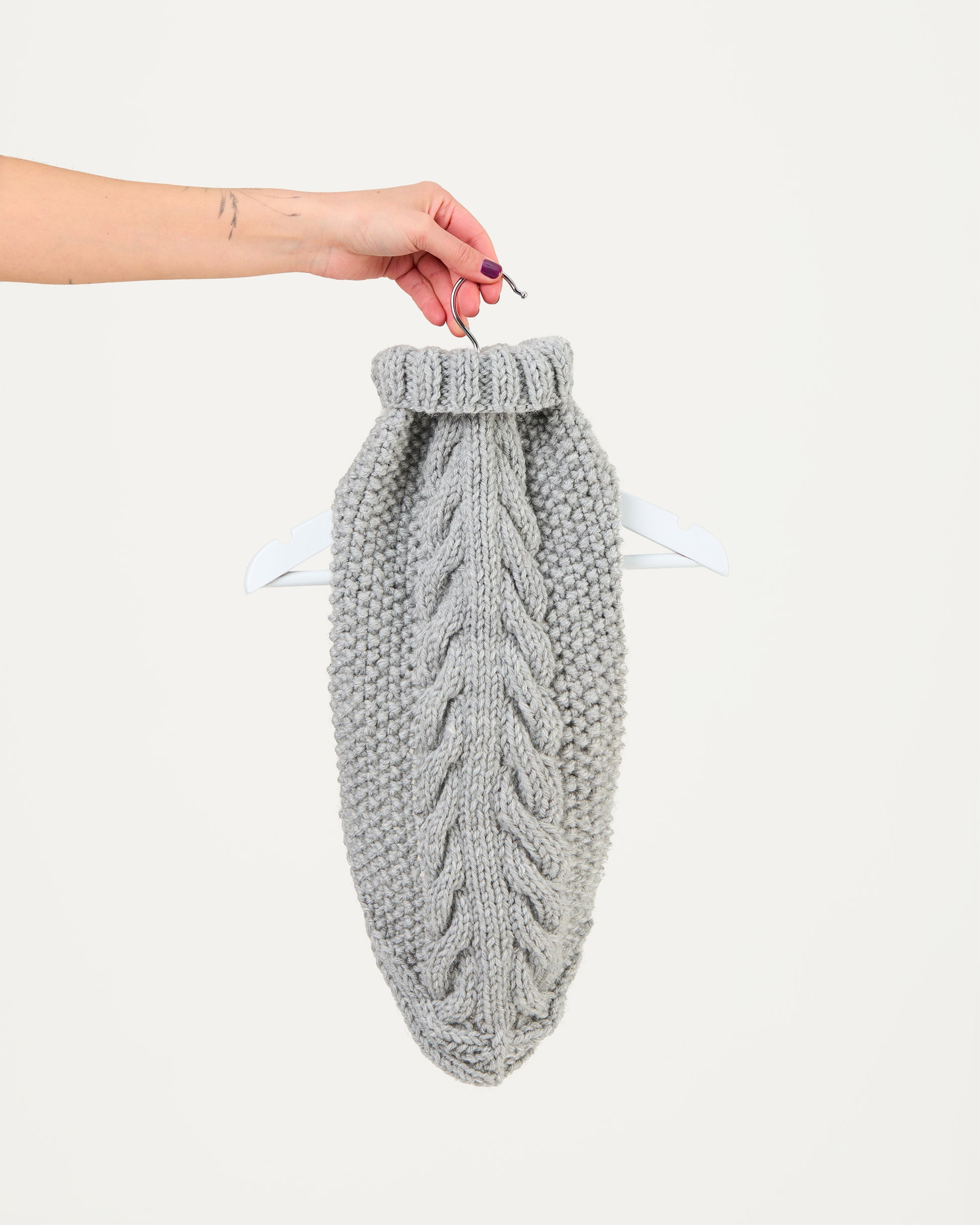 Gray knitted dog jumper held by a hand on a white background
