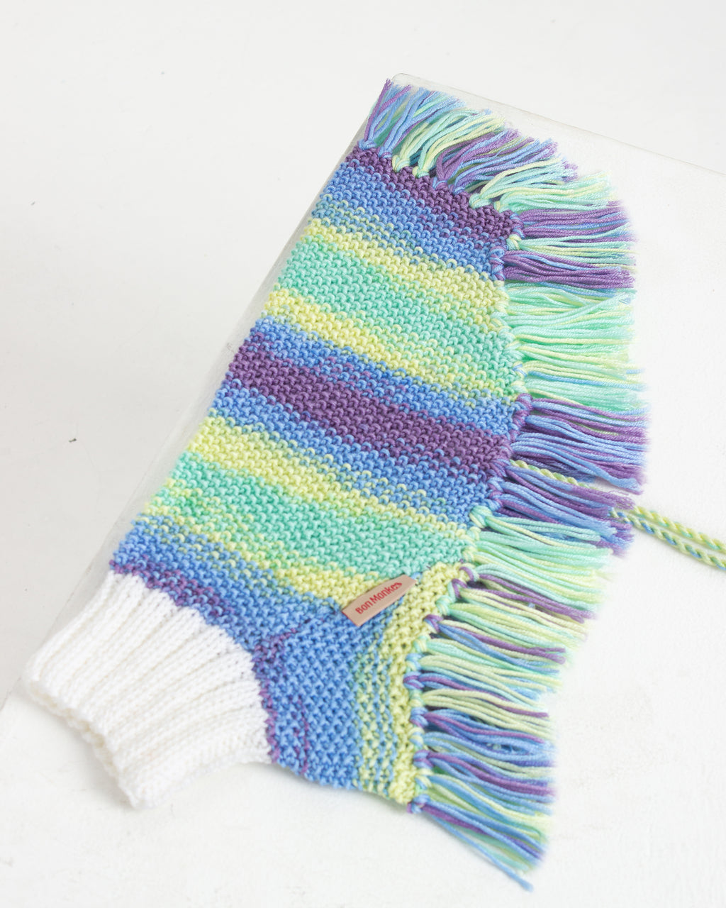 Colorful knitted dog poncho with fringes on a white background